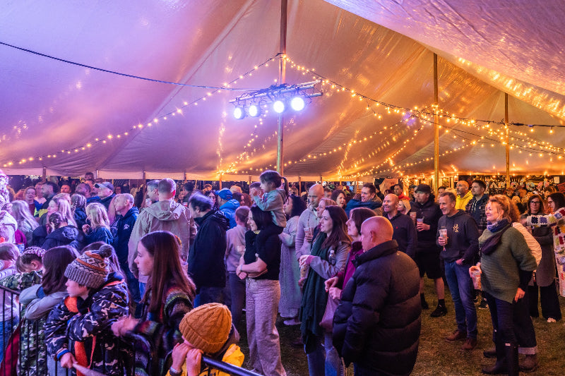 Festival-goers gathered under the marquee at Glampfest with string lights at night.