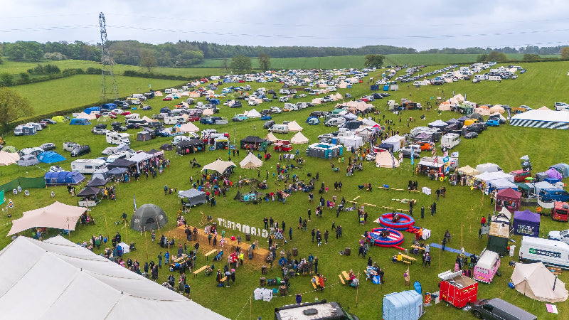 Aerial view of Glampfest family festival with tents, cars, and people enjoyin ghte activities under a clear sky.