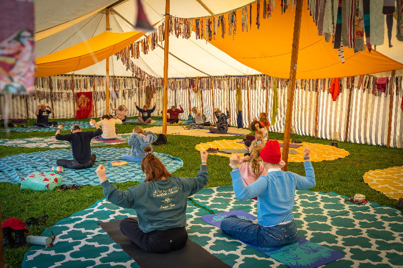 Group of people practicing yoga at Glampfest festival Knaresborough under a large tent with colourful decorations.