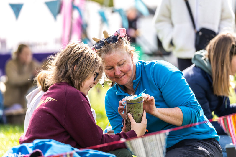 Two women sitting on grass doing forest school activities at Glampfest family festival in Knaresborough.