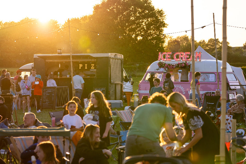 People gathered around food trucks Glampfest family festival in Yorkshire with trees in the background